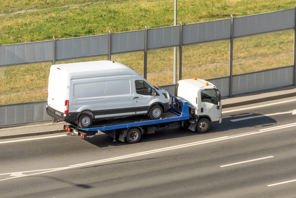 A tow truck carries a delivery van to the repair shop after a crash that occurred due to driver distraction, one of the most common causes of collisions involving delivery vans.