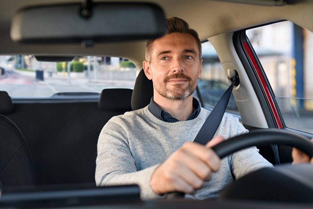 A man checks his rearview mirror and smiles. The purpose of the rearview mirror is to see what is happening behind your car.